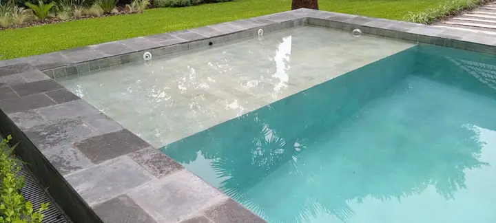 Borde de piedra gris sobre piscina de agua cristalina