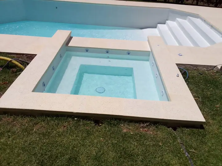 Jacuzzi de hormigón de 2 por 2 metros revestido en venecita blanca junto a la piscina