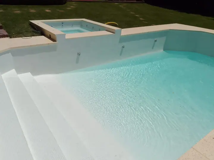 Jacuzzi elevado de hormigón integrado a una piscina clara