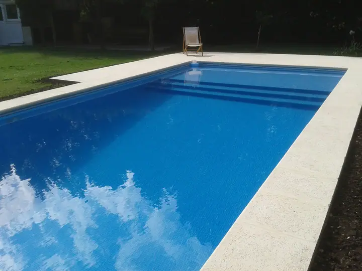 Piscina rectangular de 10 por 4 metros revestida en venecita azul, con borde y solárium claros