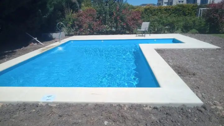 Piscina con borde claro y solárium en jardín con plantas