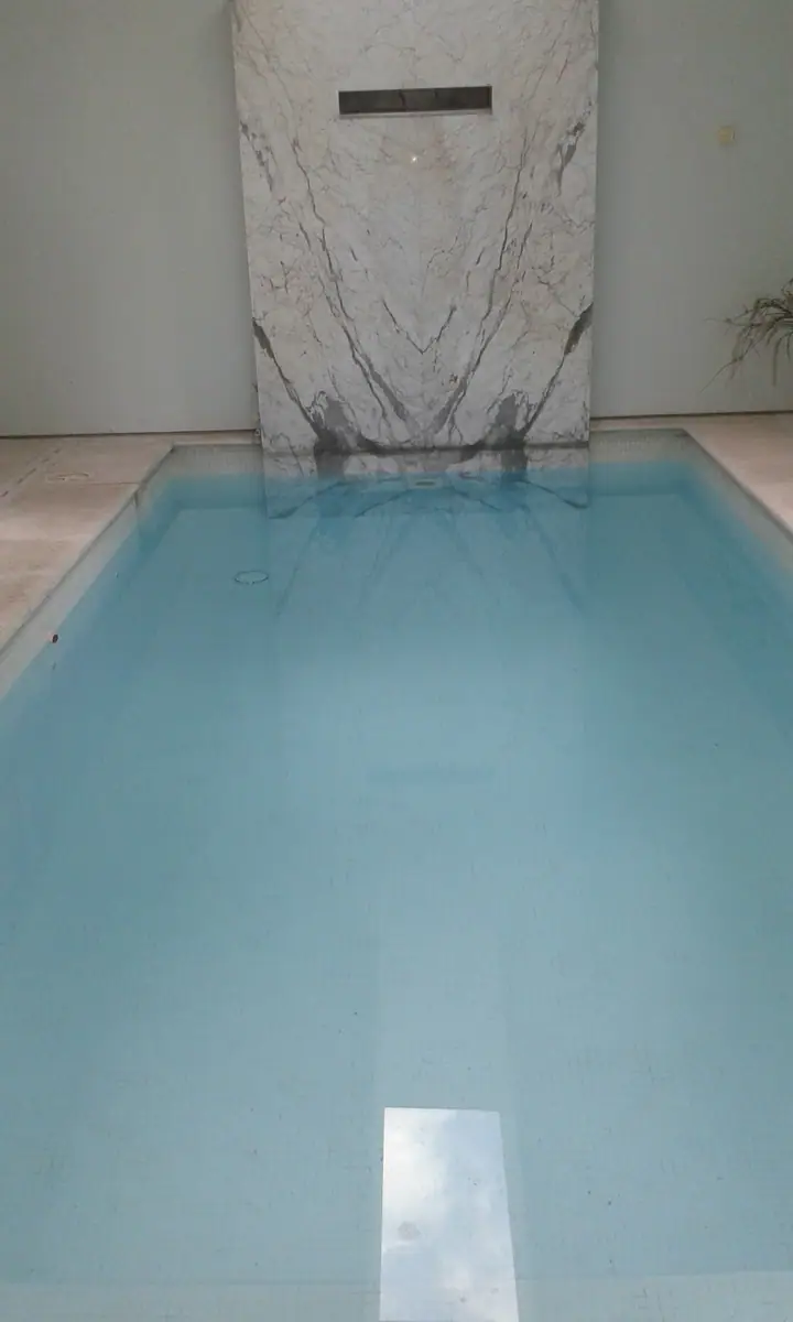 Piscina cubierta con agua cristalina y pared revestida en mármol