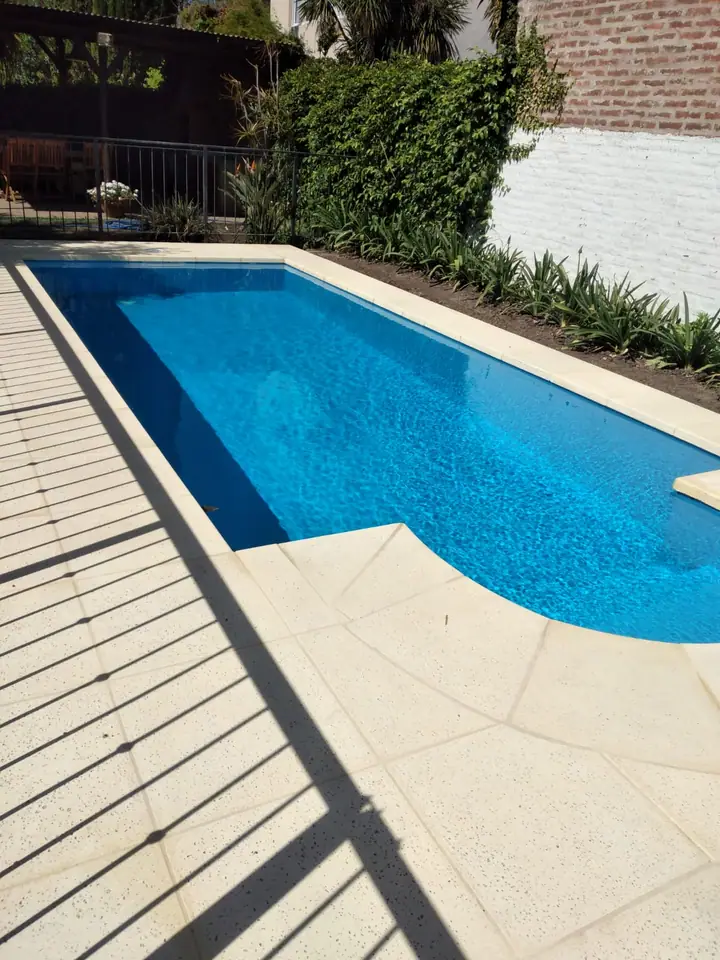 Piscina con escalones de ingreso curvos, deck de madera y cerco verde