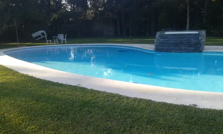 Piscina de forma libre con cascada de piedra y borde claro sobre el césped