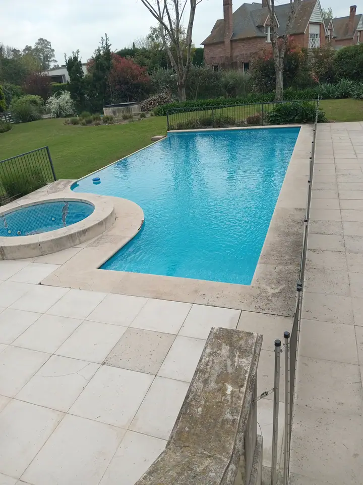 Piscina rectangular con jacuzzi circular integrado y solárium de placas claras