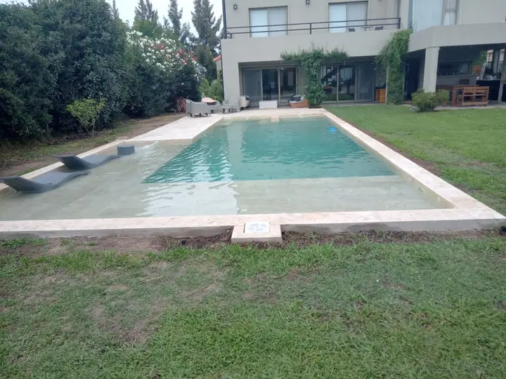 Piscina terminada en el jardín de una vivienda, con solárium claro y césped