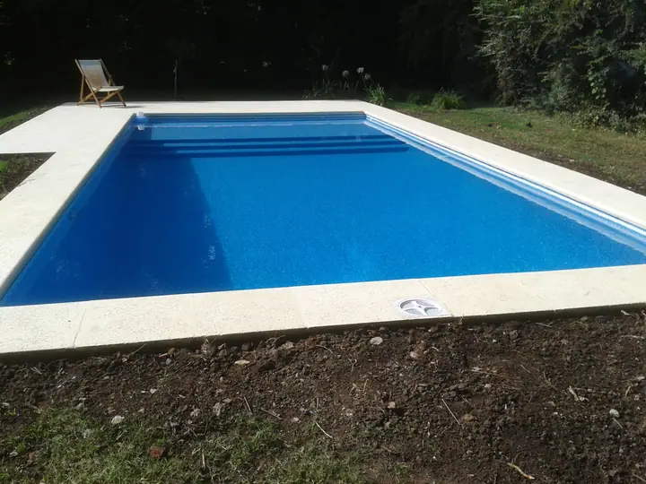 Piscina rectangular azul con escalera de obra y borde claro sobre el césped