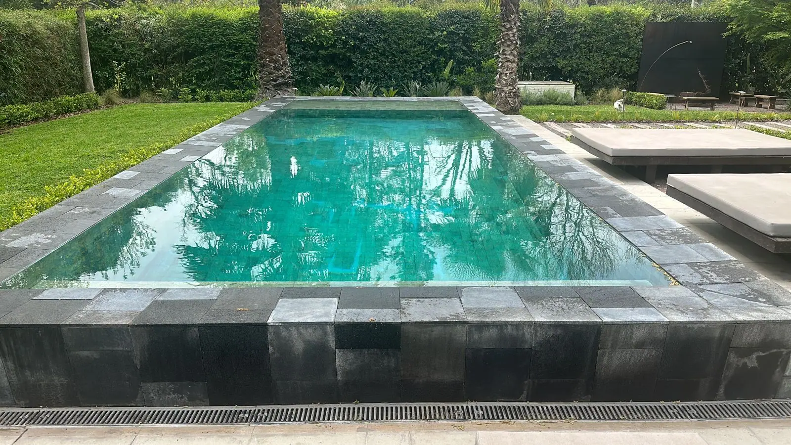 Piscina refaccionada con borde de piedra oscura, agua verde esmeralda y palmeras