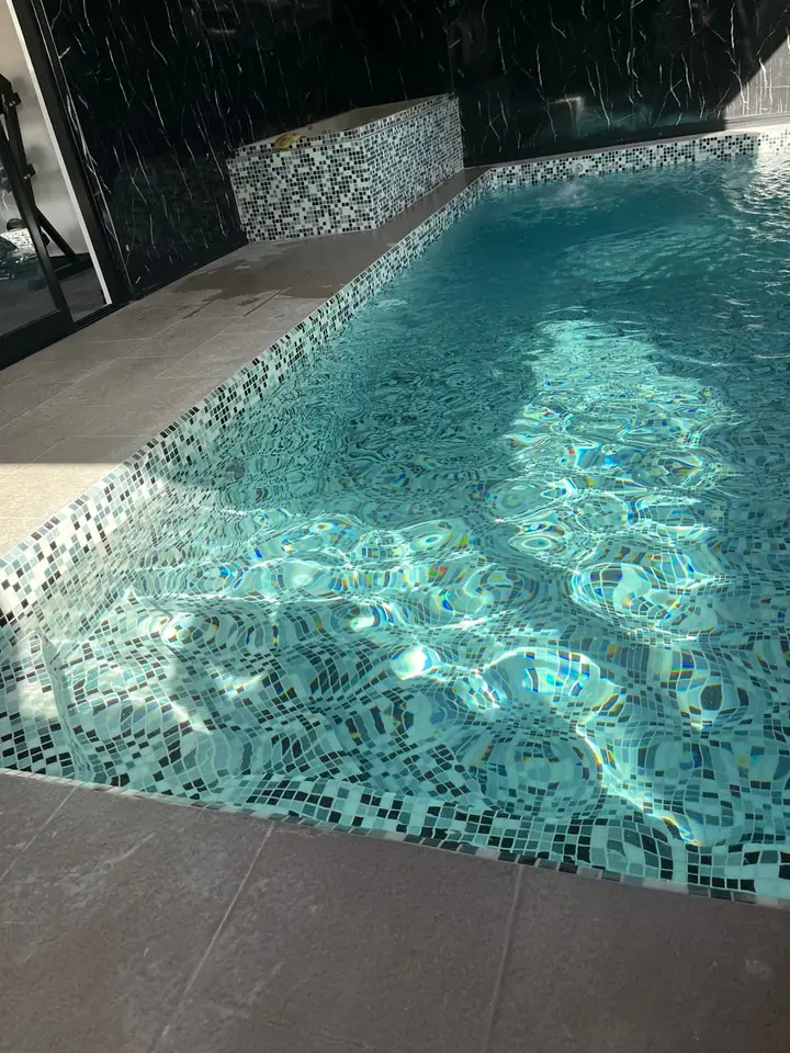 Fondo de piscina en venecita turquesa con reflejos de sol sobre el agua
